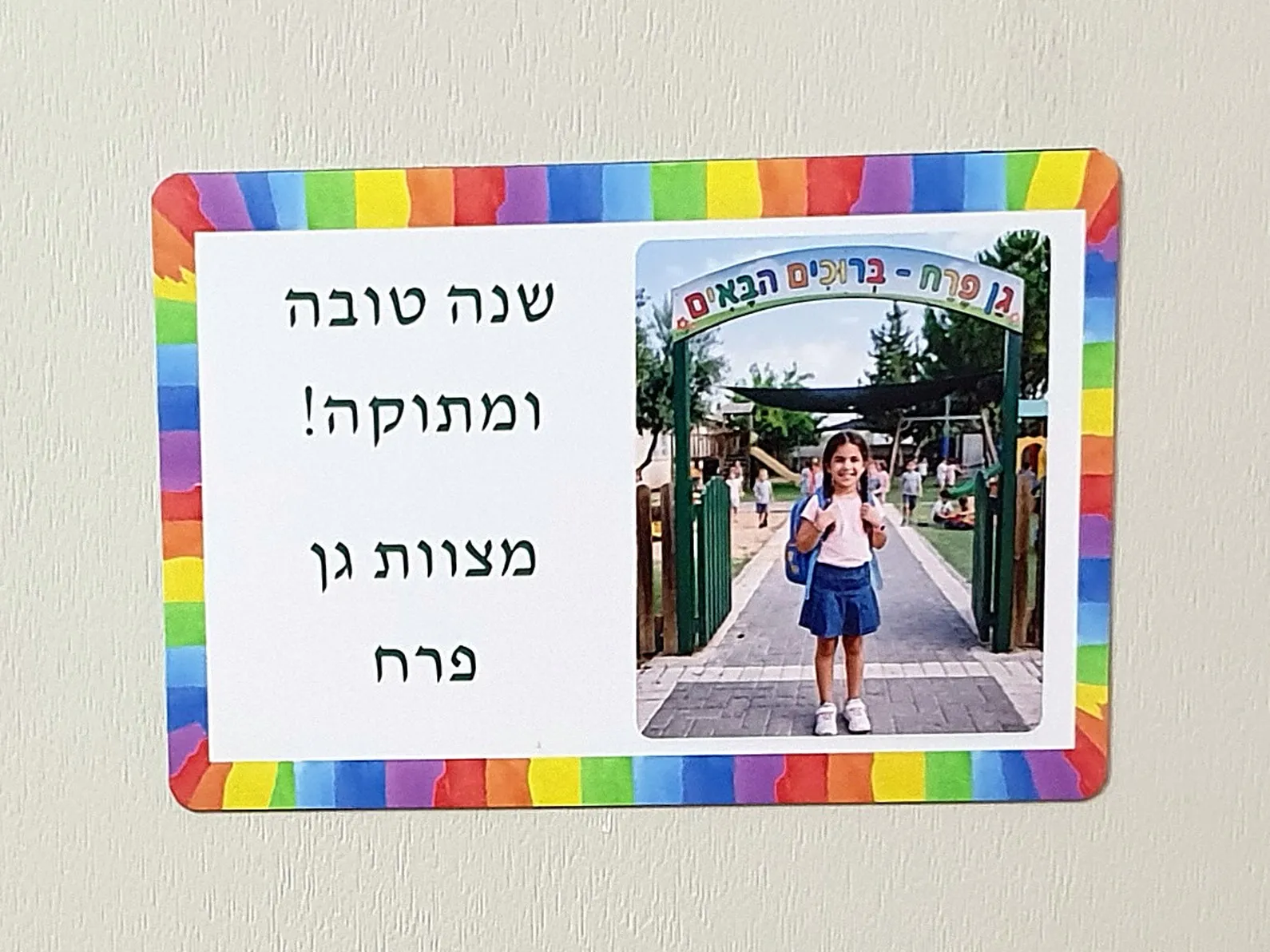 מגנט עם ברכת שנה טובה ותמונת ילדה בכניסה לגן, במסגרת צבעונית על דלת
